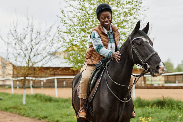 Woman Riding Horse at Country Farm Portrait of smiling black woman riding horse in outdoor country ranch and stroking gently, copy space all horse riding stock pictures, royalty-free photos & images