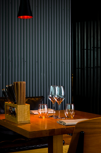 Asian restaurant with dark modern interiors and sustainable wooden furniture with table setting for two with vertical rectilinear lines on the wall