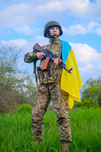 Soldado de cuerpo entero con arma y bandera ucraniana en el hombro mirando hacia otro lado photo