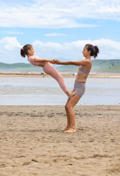 мама и дочь практикуют акройогу на пляже - yoga flexibility two people women стоковые фото и изображения