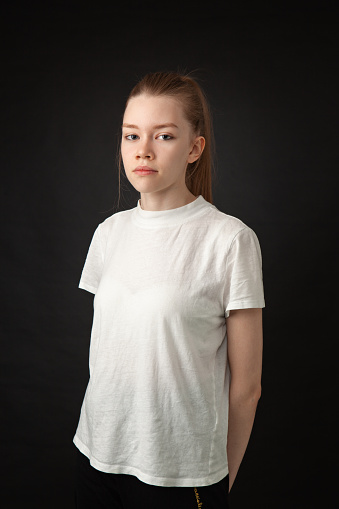 Studio portrait of a 22 year old woman with brown hair in a white t-shirt on a black background