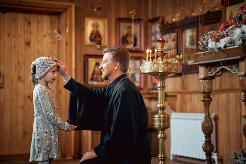 a priest blesses a little girl in a headscarf in an Orthodox church after a festive church mass.