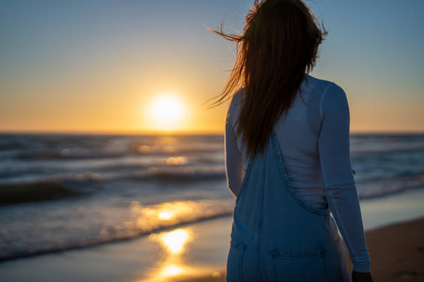 istock woman watches the sunset while walking on the beach 1408537312