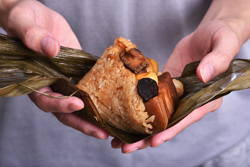 Hand holding zongzi (rice dumpling) with savoury fillings wrapped in bamboo or reed leaves.