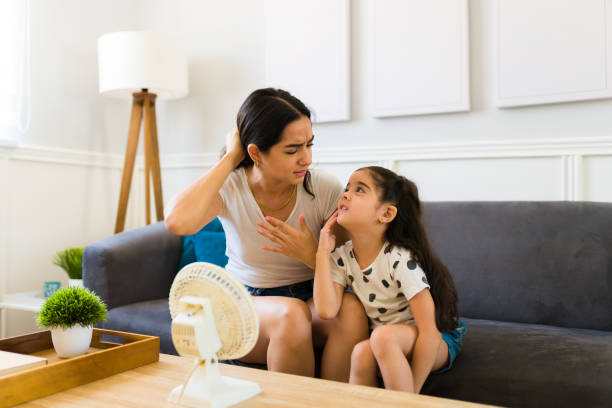 Mom and young kid feeling very hot during a heat wave at home Sweaty young woman and little kid suffering because of the hot weather and refreshing in front of the electric fan at home hot mexican girls stock pictures, royalty-free photos & images