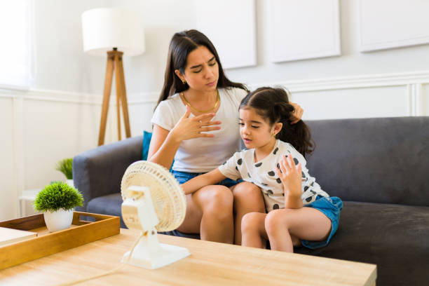 Mom and daughter turning on the fan during a heat wave at home Tired little girl and latin mom feeling very hot during the summer and sitting in front of the fan at home because of the heat weave hot mexican girls stock pictures, royalty-free photos & images