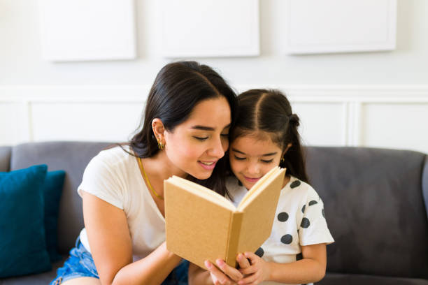 istock Latin mom and girl enjoying a book while resting on the sofa 1408548340