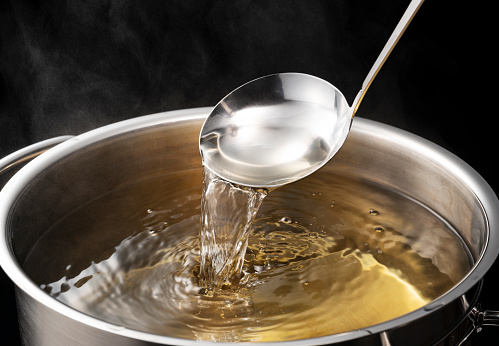 Dashi, soup stock, and the basics of Japanese cuisine. Black background. Steam. Scooping with a ladle.