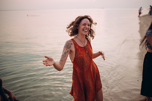 Smiling, young woman is dancing on the beach at sunset.