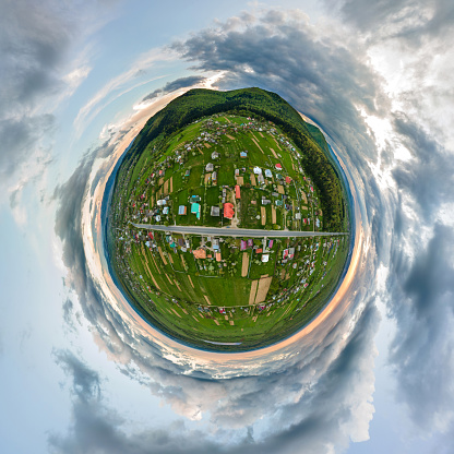 Little planet view of village houses and distant green cultivated agricultural fields with growing crops on bright summer day.