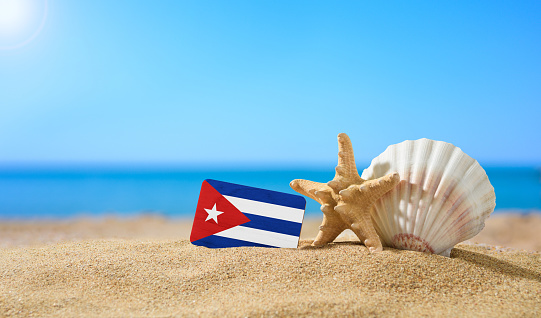 Tropical beach with seashells and Cuba flag. The concept of a paradise vacation on the beaches of Cuba.