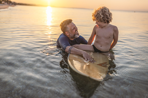 Photo of boy having fun in the sea with his father on a surfboard.