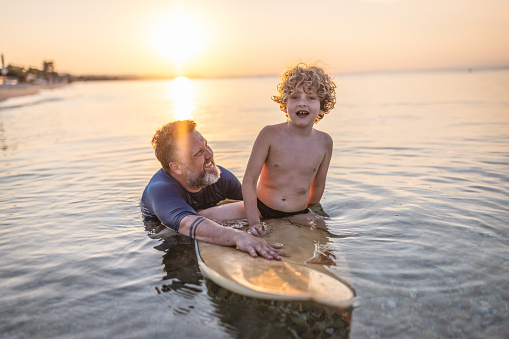 Photo of boy having fun in the sea with his father on a surfboard.