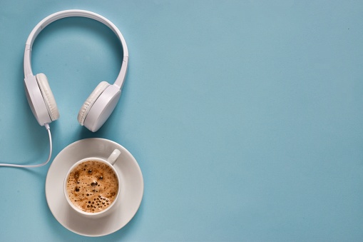 Headphones and coffee cup on a light blue background. Top view. Flat lay composition with copy space