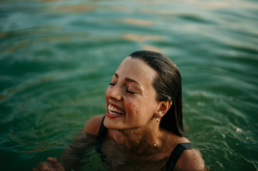 Spontaneous close up image of a beautiful young adult woman, a brunet, enjoying the sea with a big smile on her face