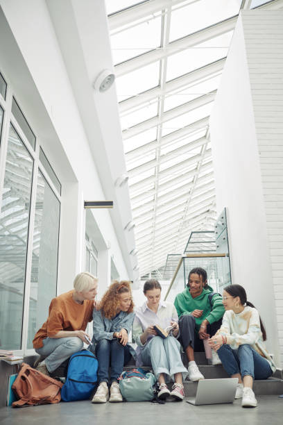 istock Five intercultural teenage classmates reading book or textbook at break 1408572478