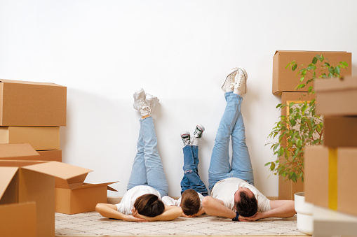 Happy family lying on the floor in new home with cordboard boxes around, close up