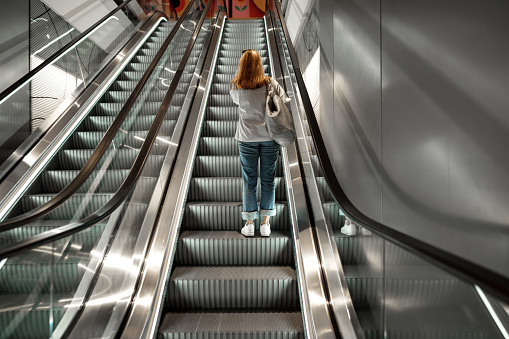 Back view of a woman standing on escalator going up