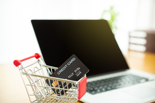Luxury black credit card in the small chopping cart with modern laptop computer in background, online shopping and online payment concept. Security in e-commerce payment and transaction