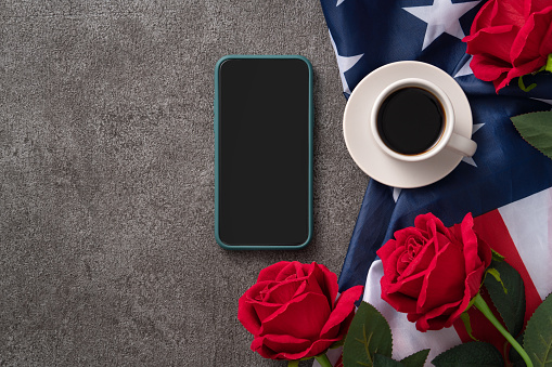 Concept of U.S Independence day or Memorial day with smart phone and a cupt of coffee. National flag over dark gray table background.