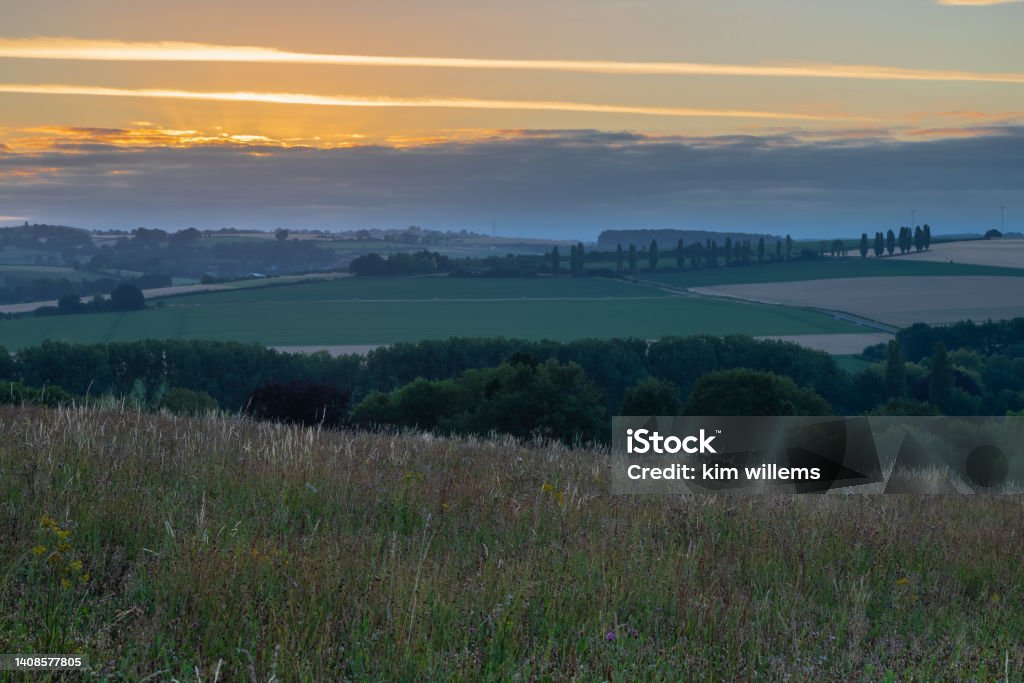 Spectacular sunrise seen from Gulpen Wittem over the rolling hill landscape in the south of Limburg over the villages of Eys and the Eyser Plantage and the poplar trees Spectacular sunrise seen from Gulpen Wittem over the rolling hill landscape in the south of Limburg with a view on the meadows and on a row of poplar trees, creating the feeling of being in the Siena Province of Italy. Agricultural Field Stock Photo