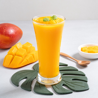 Fresh beautiful delicious mango juice. Close up design concept of smoothie cold drink in glass cup with glass straw on gray table background.