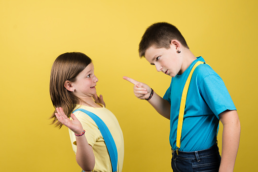 Boy bullying little girl isolated on yellow background.