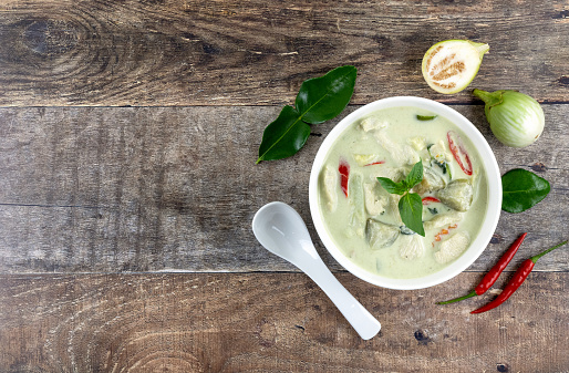 Thai traditional food - green curry with chicken, eggplant, basil, chili, on a wooden background, top view.