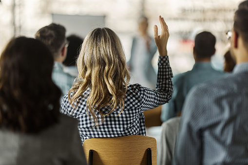 Rear view of a businesswoman raising her hand to ask the question on a seminar in board room.