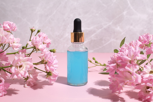 Nature cosmetic in glass bottle with flowers on pink background. Face and body care spa concept