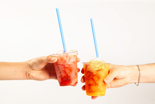 Hands holding two flavoured slush frozen drinks with straws