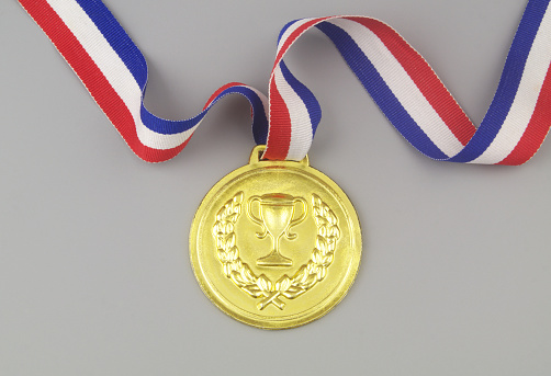 Gold medal with multicolored ribbon and trophy cup symbol on gray background