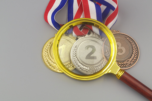 Gold, silver and bronze medals with magnifying glass. Checking competition results concept.