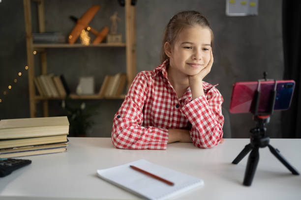 istock girl student studying online at home, looking at phone screen, watching webinar, using smartphone on tripod, writing notes, homeschooling 1408590962