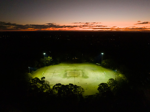 Aerial view of a lit up Public Sports Field Oval at night, with moody dusk sky.  Public Park - Parklands Oval, Mount Colah Sydney NSW, Australia