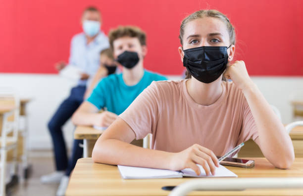 istock Young students in face masks sitting at desks in classroom 1408593624