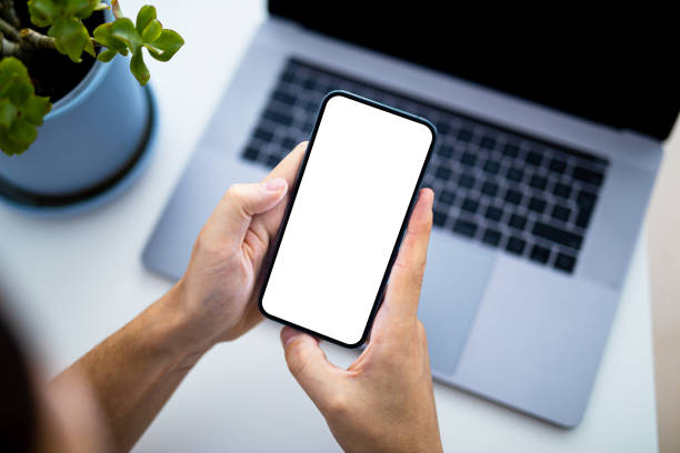 istock Man using smartphone blank screen frameless modern  - top view, laptop keyboard in background 1408594056