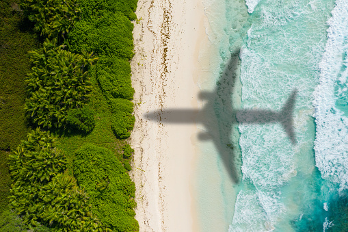 Shadow of passenger aircraft flying over sand beach of tropical island on sunny vacation day