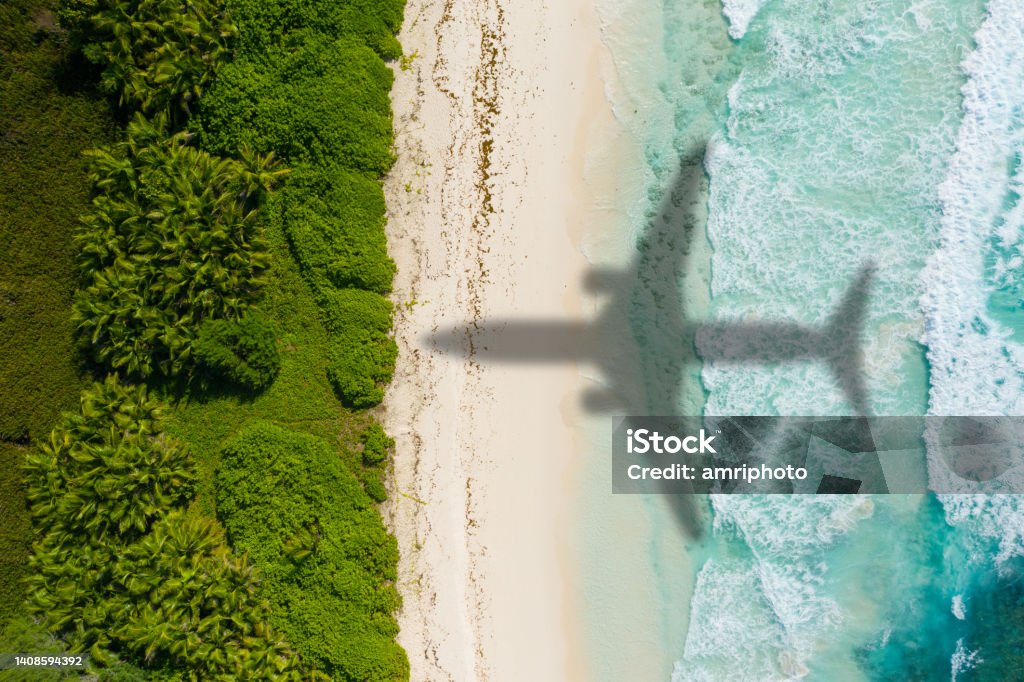Airplaine arriving on tropical holiday destination. Vacation concept Shadow of passenger aircraft flying over sand beach of tropical island on sunny vacation day Airplane Stock Photo