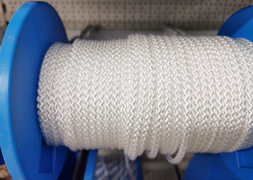 Receding row of cashmere wool on conical spools in shades of green, grey and white at a knitwear factory with focus to a reel of green yarn in the center