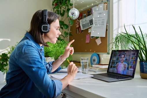 Female teacher in headphones teaching young student girl online. Sitting at home, high school teen pupil at laptop screen, talking female using video call chat conference. E-learning, remote lesson