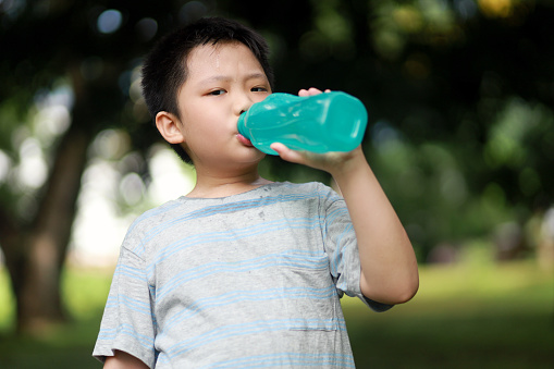 Boy drinking water from plastic bottle at a park after playing badminton