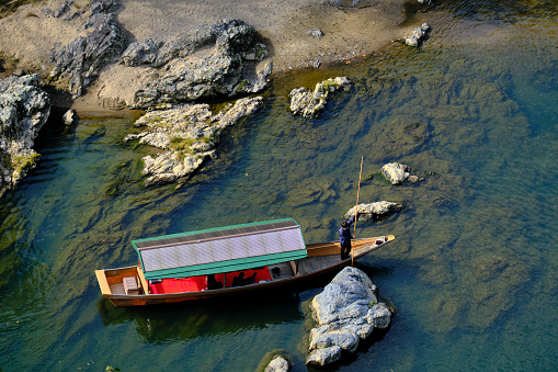Kyoto, Japan - November 19, 2021: A boatman steers a wooden vessel around a large rock in the Hozu River. Visitors to the Arashiyama area can ride the boats down the winding river through the Hozu Ravine to take in the picturesque scenery.
