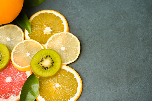 Healthy Food Background. Sliced fruits on a gray stone background. Citrus, orange, lemon, kiwi grapefruit, green leaves. Raw food diet.