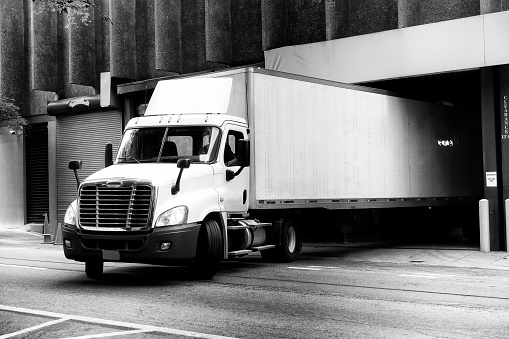 The semi truck with box trailer leaves the gate of multi story building after unloading the delivered cargo. Atlanta, Georgia, USA.