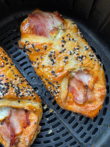 Stock photo showing close-up, elevated view of the inside of an air fryer with freshly baked, pastry wraps filled with bacon and cheese. Healthy cooking concept.