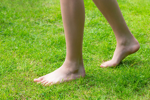 Barefoot feet walking on fresh green grass lawn in summer