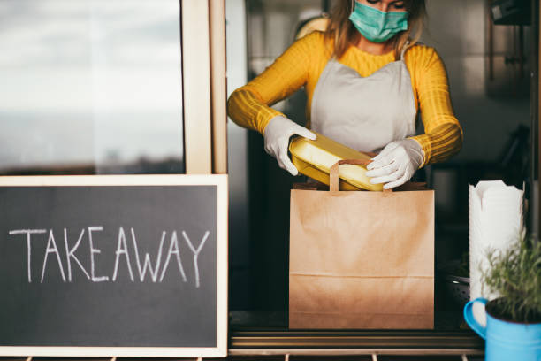 istock Young woman preparing takeaway food inside restaurant during Coronavirus outbreak - Focus on right hand holding bag 1408613615