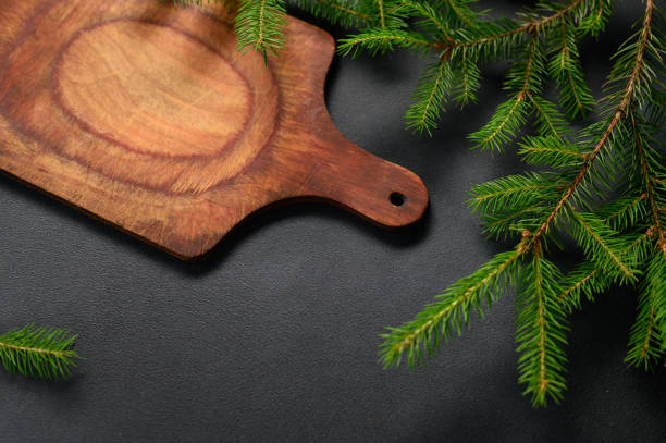 istock Top View Black Textured Table with Green Branches and Empty Cutting Board. Old Wooden Cheese Board 1408613688