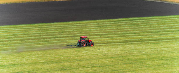 istock Red tractor mowing on green cultivated agriculture green field, panoramic image 1408614852